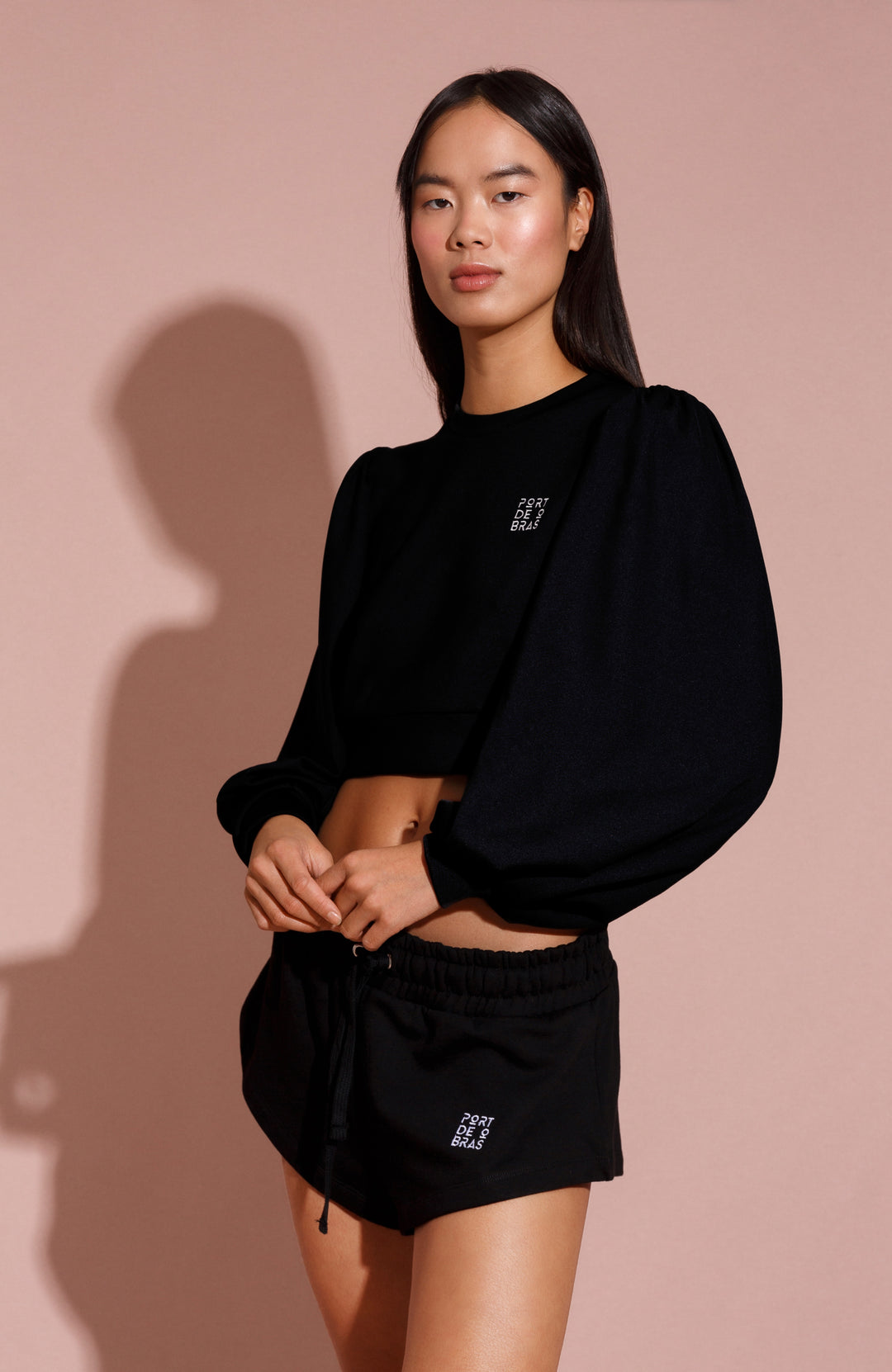 Person wearing a black outfit with a logo on a pink background