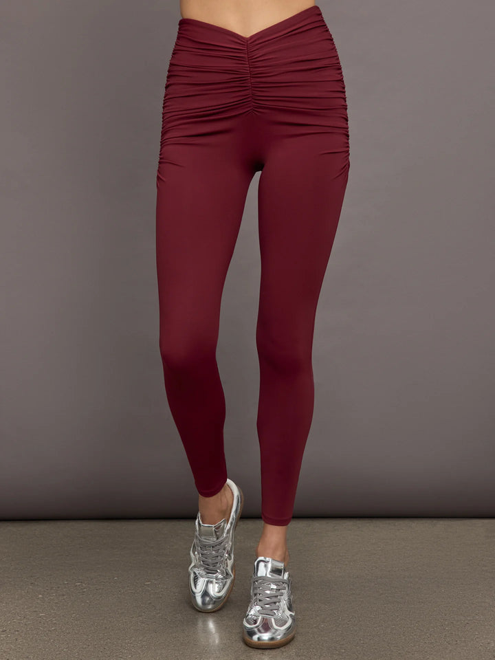 A pair of burgundy leggings with a ruched waist, worn with silver athletic shoes.