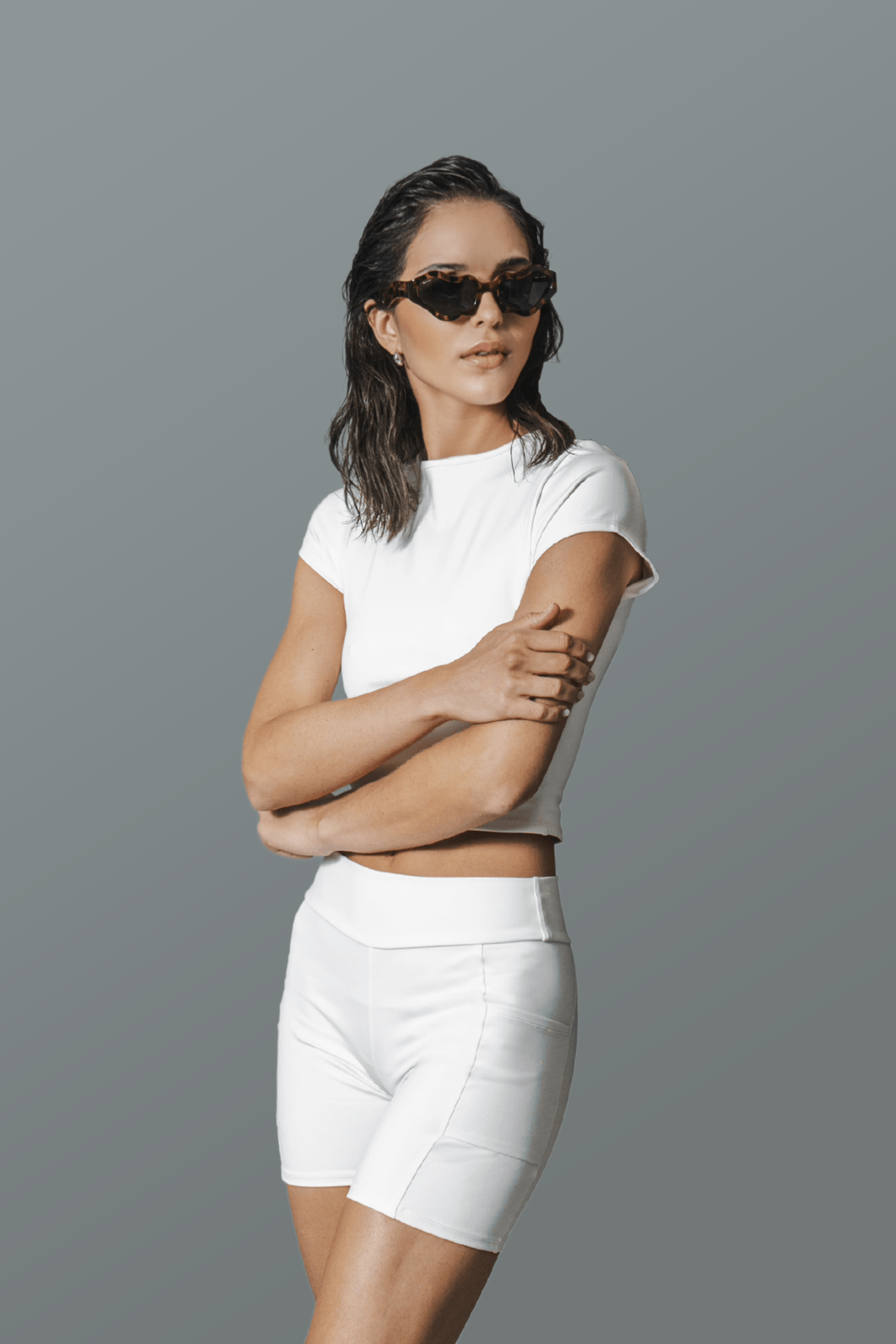 Woman wearing a white outfit with sunglasses on a gray background