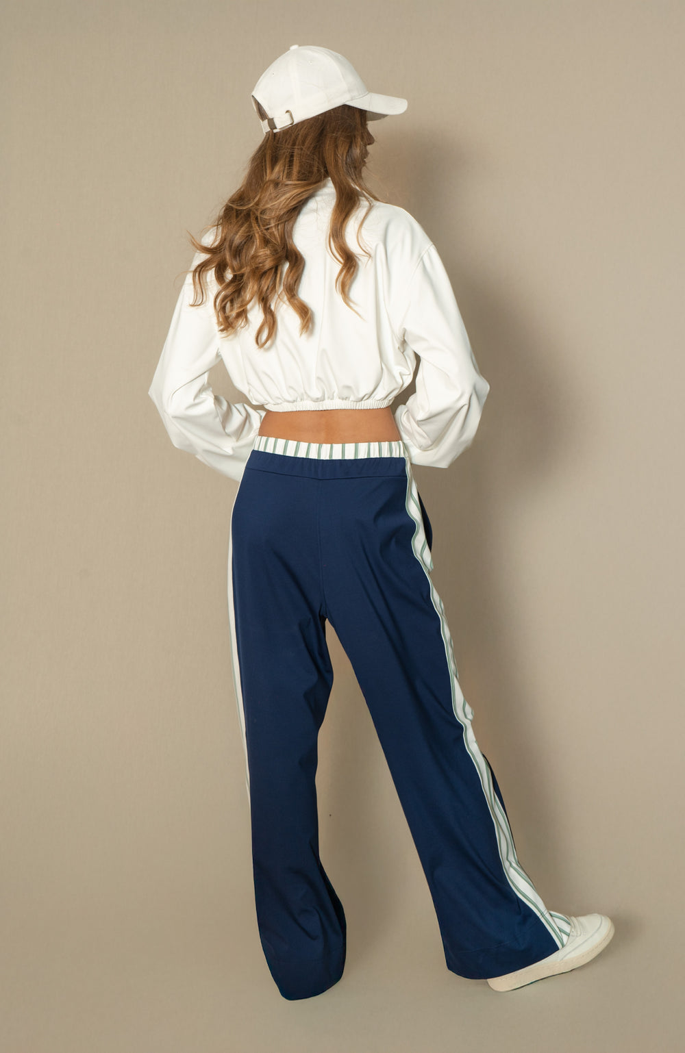 Person wearing a white shirt and navy pants with a white cap on a beige background