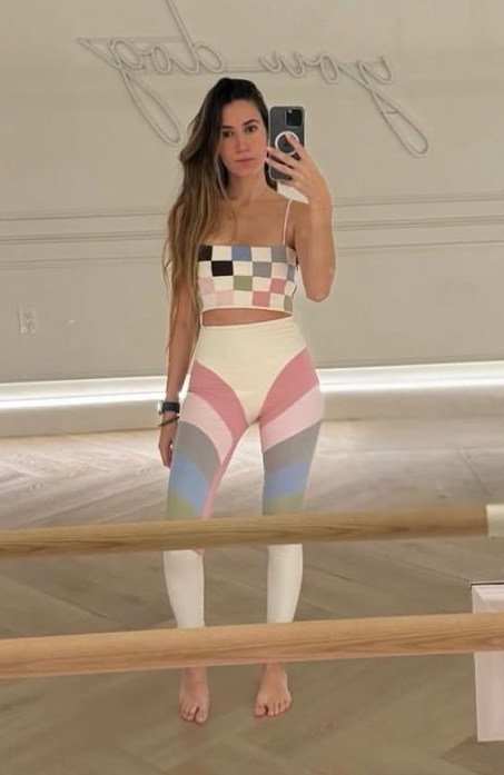 Woman taking a mirror selfie wearing a colorful checkered top and leggings.