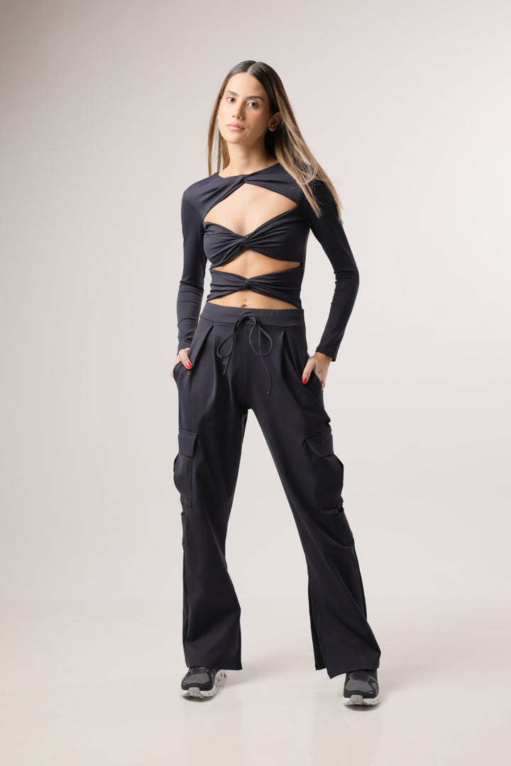 A woman standing in a studio setting, wearing black slit cargo pants with pockets on the side.
