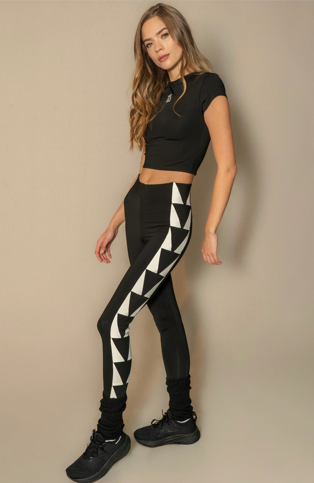 Woman wearing a black crop top and black leggings with white triangle pattern on a beige background