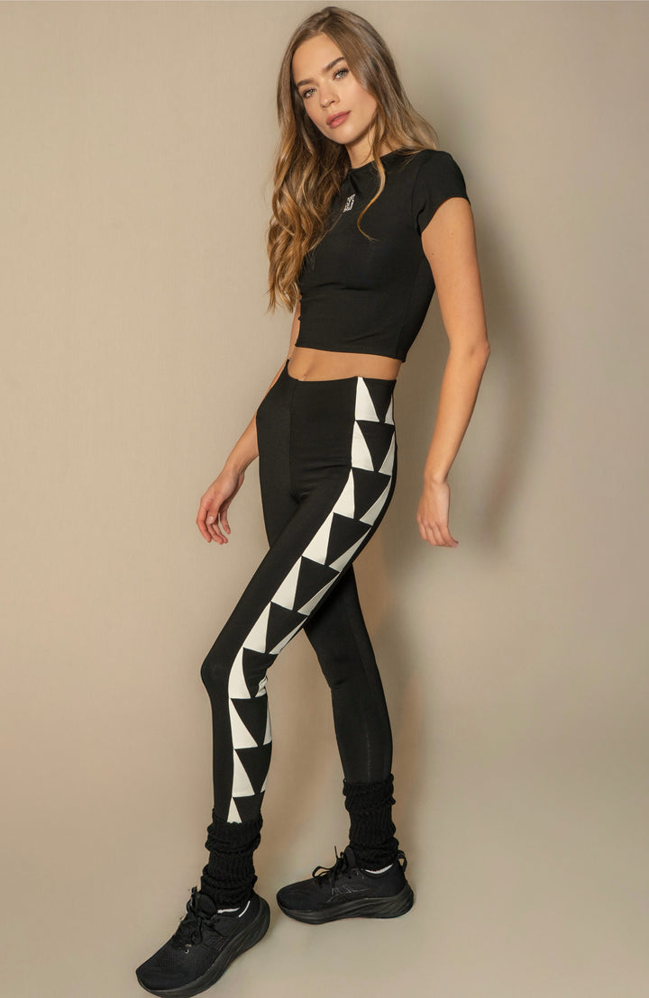 Woman wearing a black crop top and black leggings with white triangle pattern on a beige background