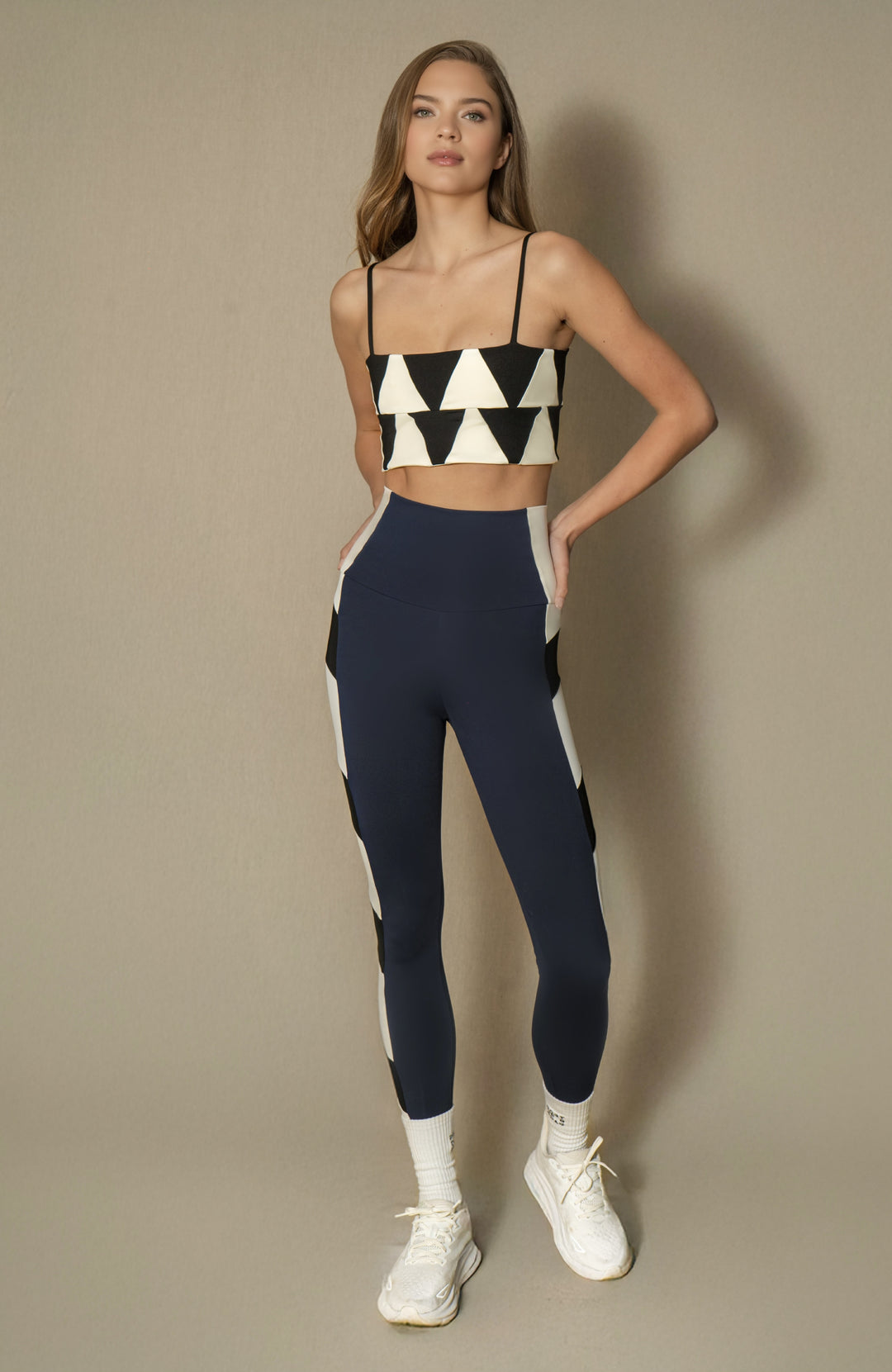 Woman wearing a black and white geometric sports bra and navy leggings with white accents on a beige background