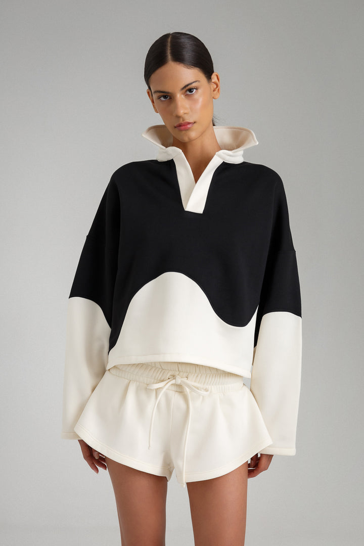 Model wearing a black and white outfit with a high collar on a gray background