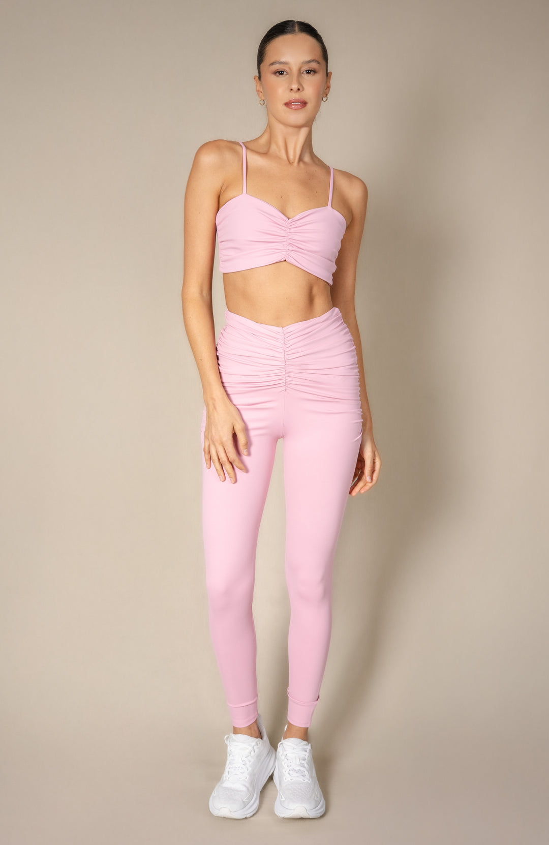 Woman wearing a pink sports bra and leggings set against a beige background