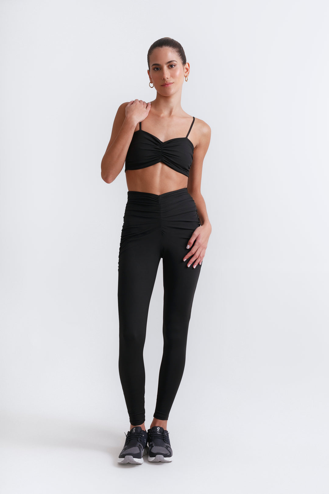 A woman is standing, wearing a black top with a cut-out design at the front and black leggings.
