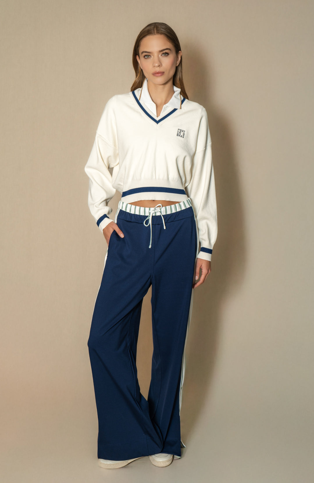 Woman wearing a white top and blue pants against a beige background