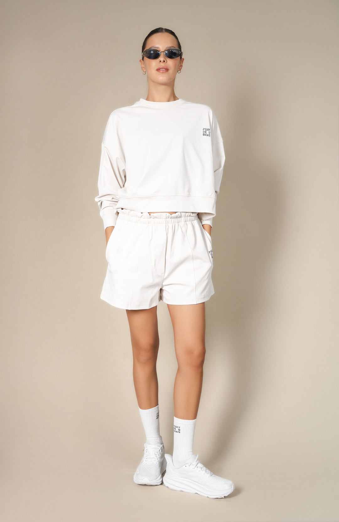 Person wearing a white sweatshirt, shorts, and sneakers on a beige background
