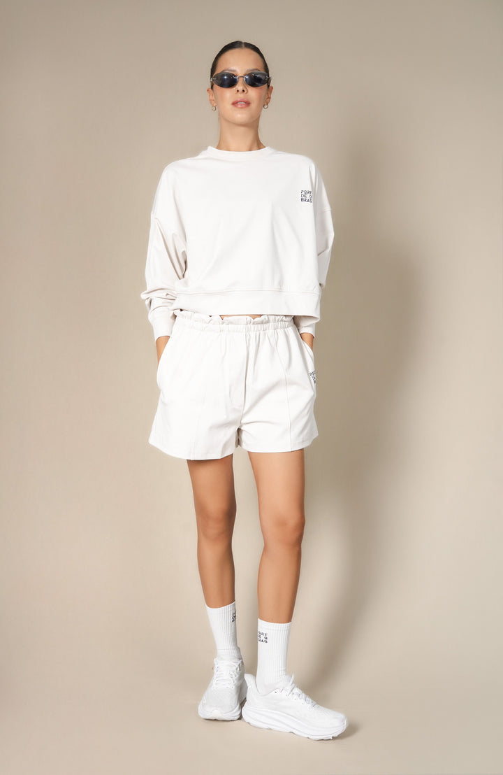 Person wearing a white sweatshirt, shorts, and sneakers on a beige background