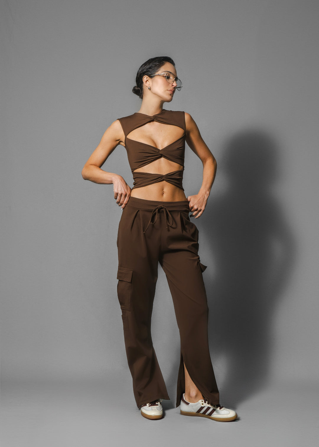 A model wearing dark chocolate brown cargo pants with a unique slit at the ankle, paired with a sleeveless top.