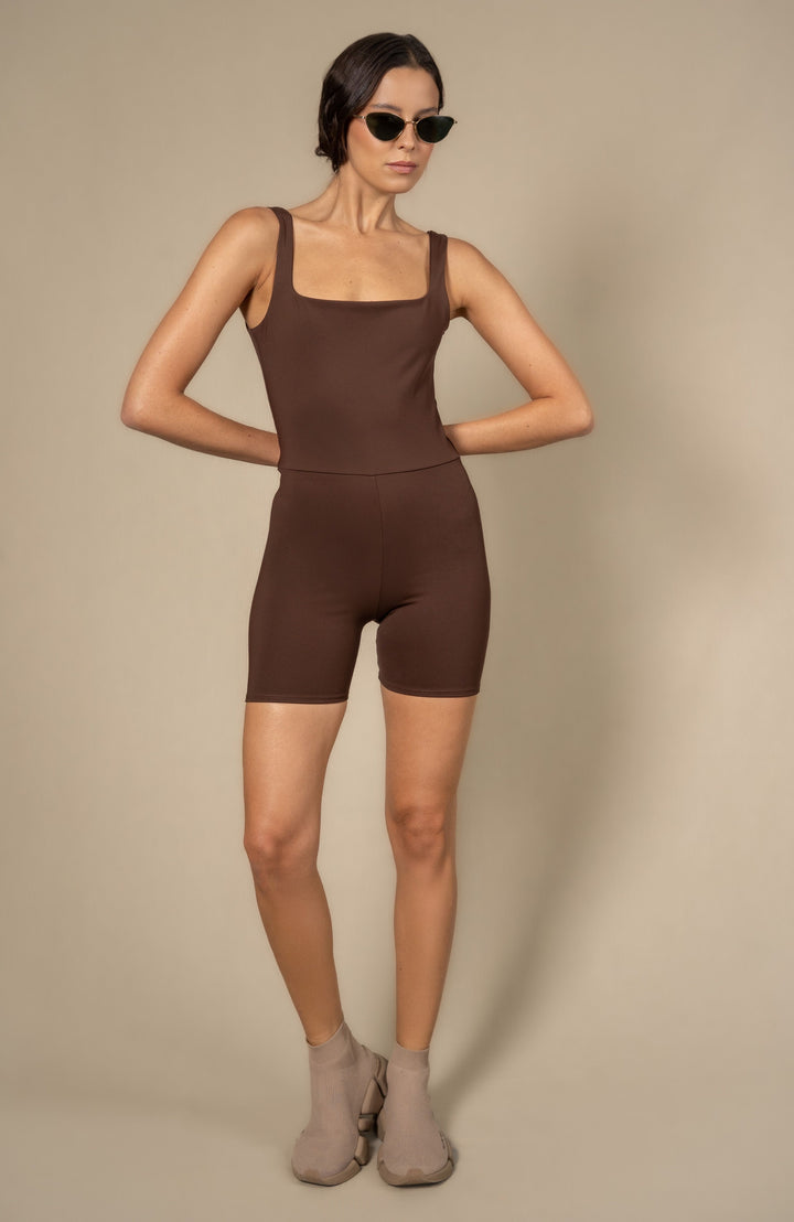 Woman wearing a brown sleeveless jumpsuit against a beige background