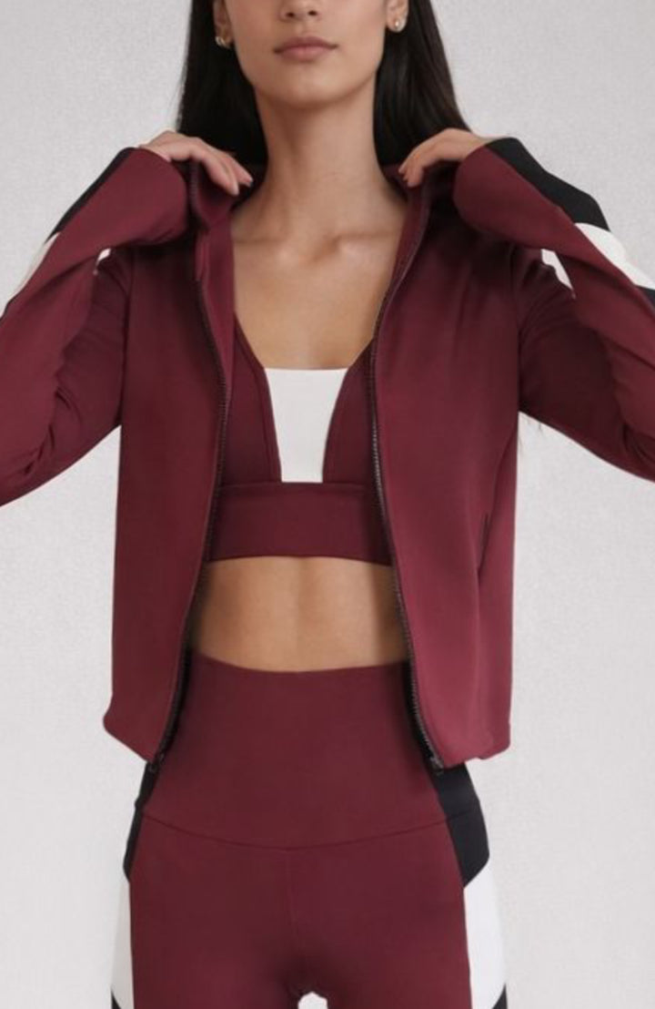 Person wearing a burgundy athletic jacket and leggings with a white top on a light gray background
