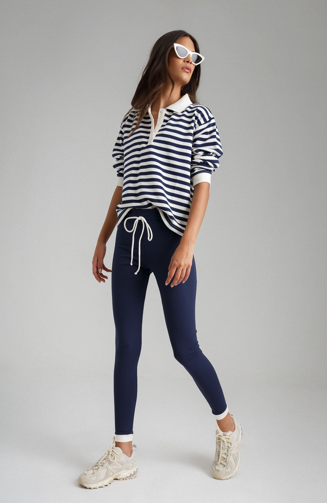 Woman wearing a striped shirt and navy leggings on a gray background