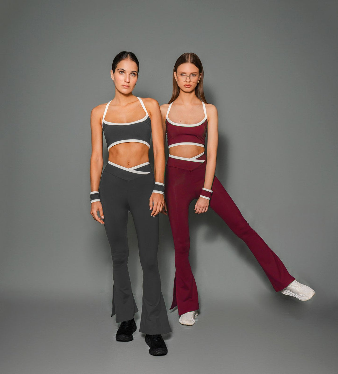 Two models wearing sports bra and leggings. One in burgundy and the other in gray.