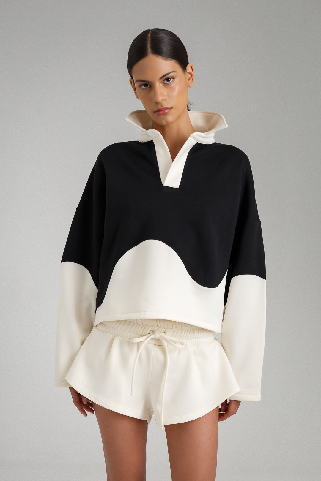Model wearing a black and white outfit with a high collar on a gray background