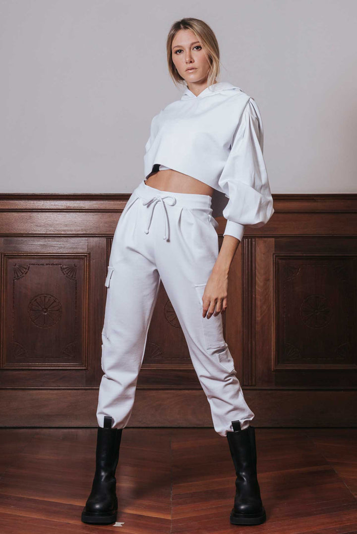 A person standing in a room with a white cargo jogger pant with a drawstring waist, paired with a hooded top and black boots.