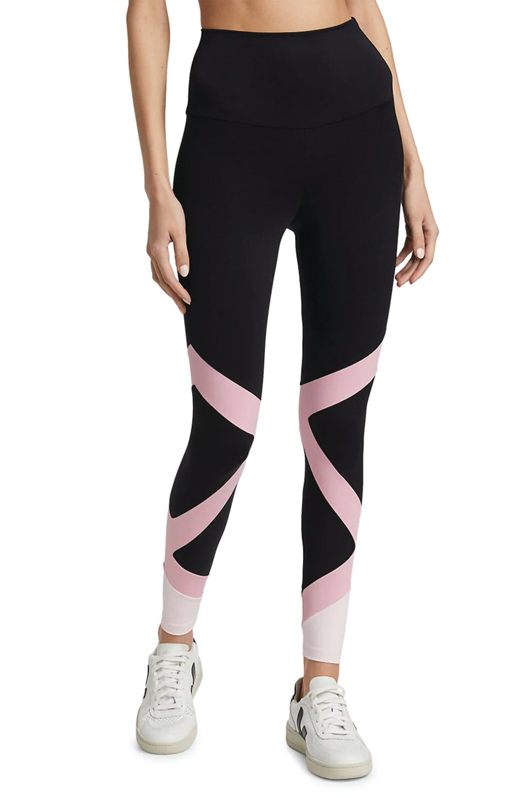 A model wearing high-waisted black leggings with pink geometric patterns, paired with white sneakers.