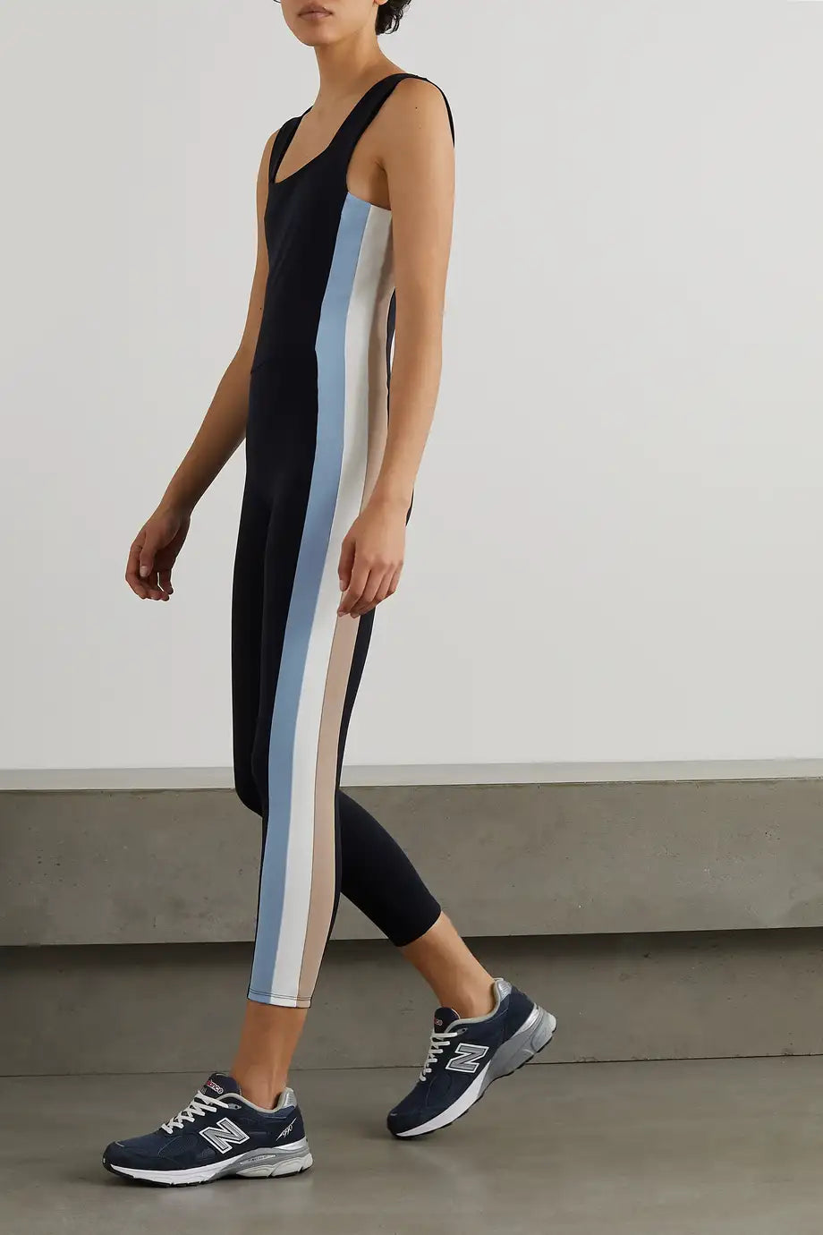 A model wearing a black unitard with a rainbow stripe design, paired with sneakers.