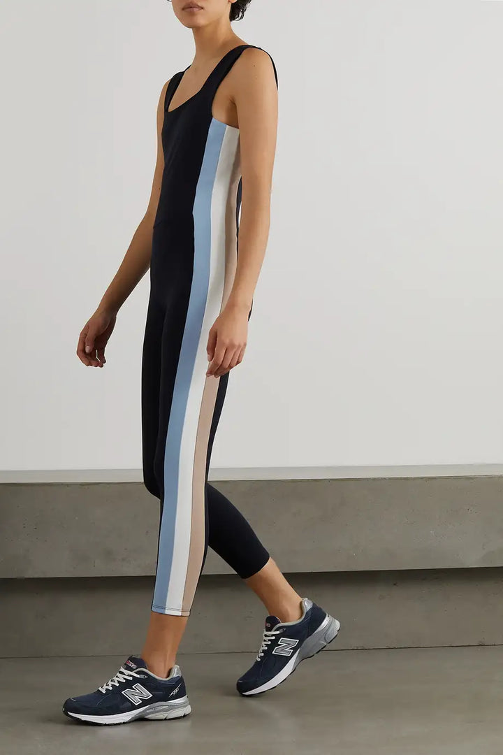A model wearing a black unitard with a rainbow stripe design, paired with sneakers.