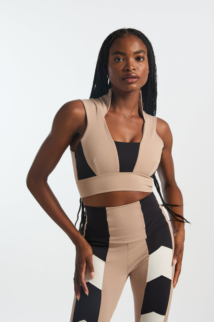 A model wearing a square neckline, high collar, sleeveless top in a pattern of beige and black shakes.